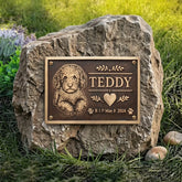 Memorial stone with a bronze plaque featuring a dog's portrait and name 'Teddy' on a grassy background.