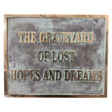 Bronze plaques with text 'The Graveyard of Lost Hopes and Dreams' on a textured surface.