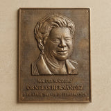 Bronze plaque with a portrait and engraved text on a beige wall