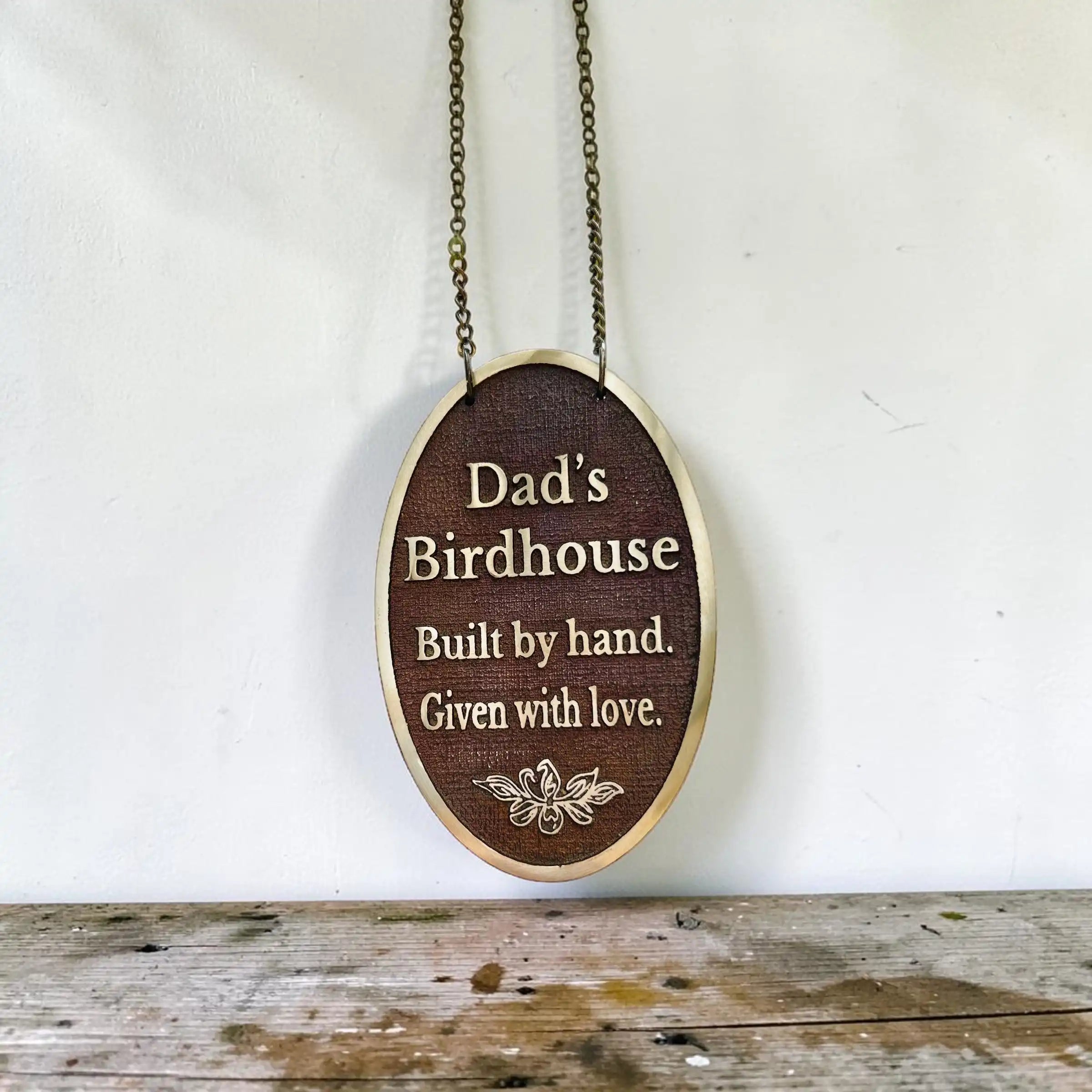 Bronze plaque with engraved text 'Dad's Birdhouse Built by hand. Given with love.' on a white background.