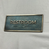 Rectangular sign with 'RESTROOM' text on a textured surface