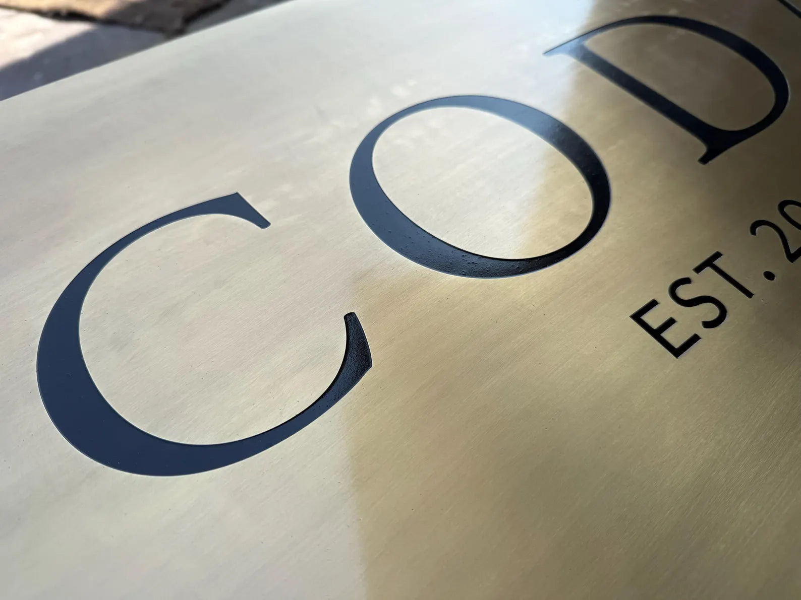Brass sign with 'COD' and 'EST. 20' text on a reflective surface