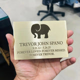 Brass Memorial plaque with elephant silhouette and text held in a hand, blurred office background