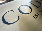 Brass sign with 'COD' and 'EST. 20' text on a reflective surface