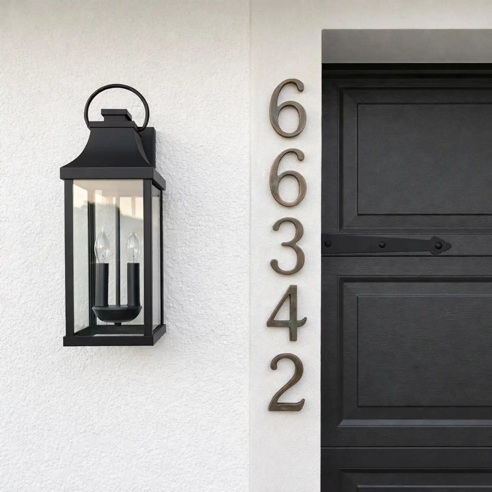Oil rubbed bronze numbers on a white wall next to a black door with house numbers.