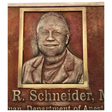 Bronze plaque with a portrait of a man and engraved text on a brown background