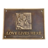 Bronze plaque with an engraving of two people and 'Love Lives Here' text on a white background