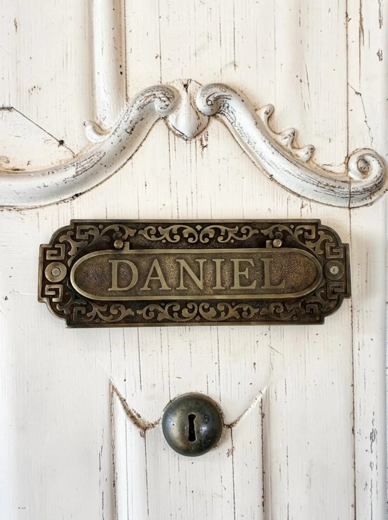 Decorative metal mail slot with 'DANIEL' on a white wooden door.