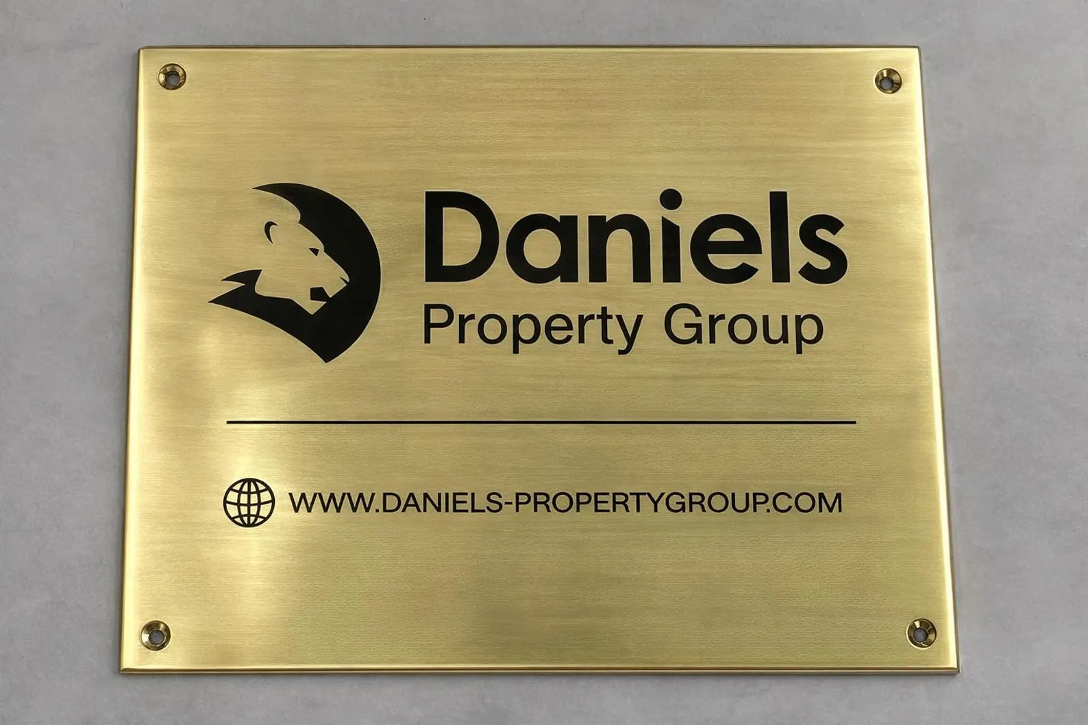 Brass plaque with Daniels Property Group logo and website on a gray background