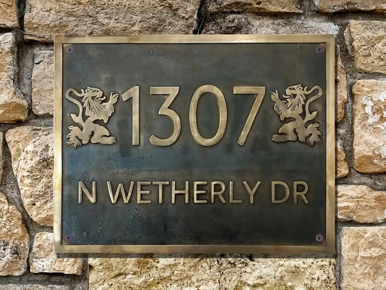Brass house number sign with '1307 N WETHERLY DR' on a stone wall.