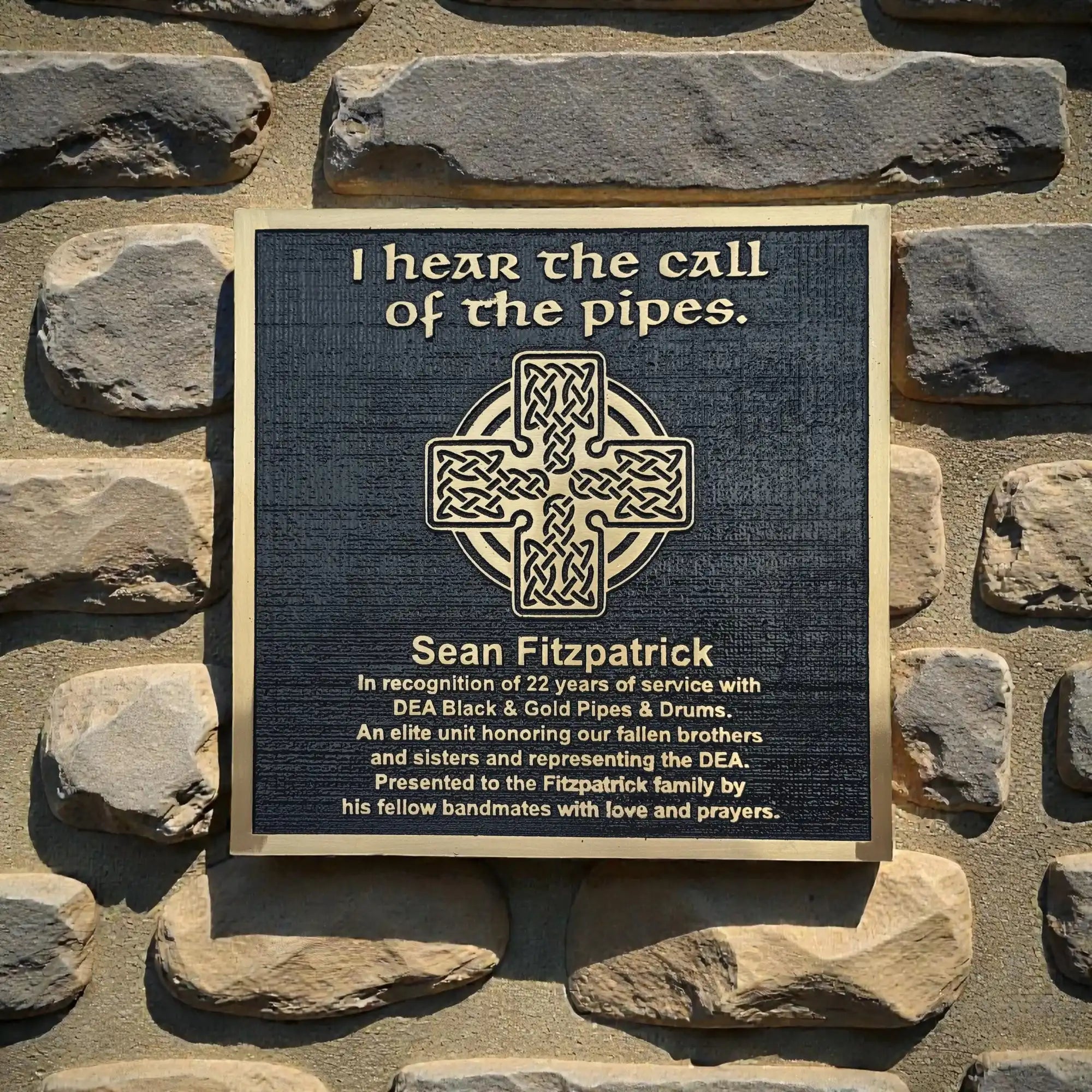 Bronze Plaque on a stone wall with text and a Celtic cross design.