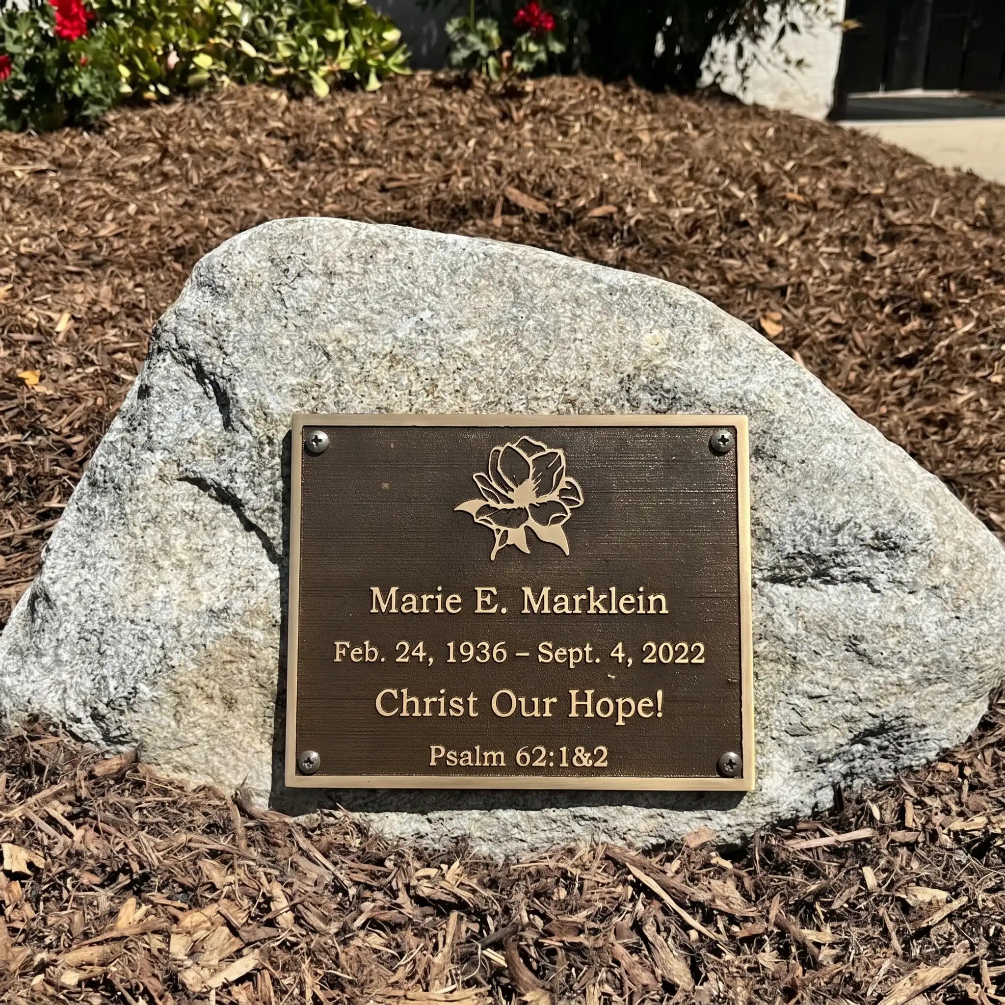 Bronze Memorial plaque on a rock with engraved text and floral design.