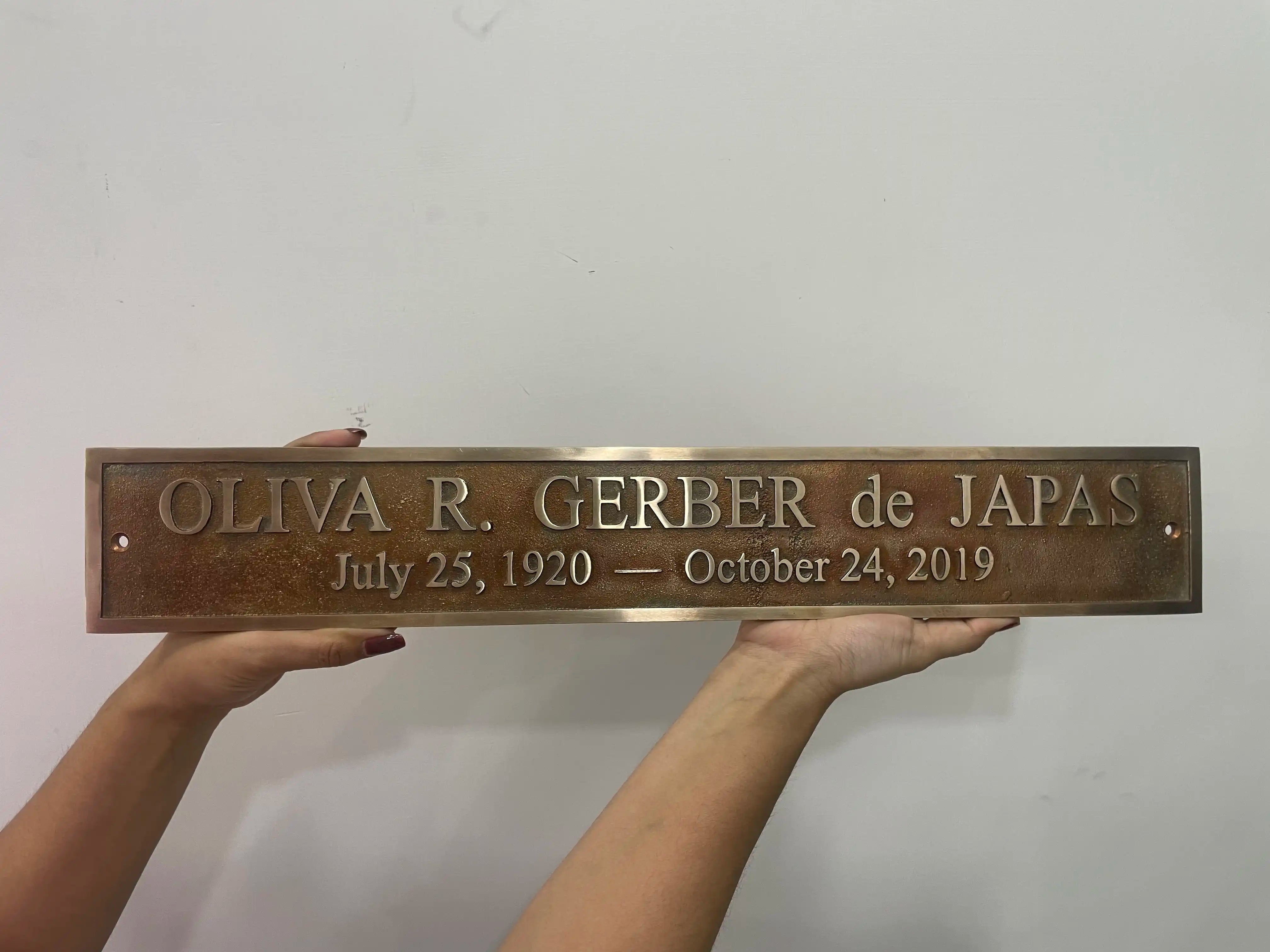 Bronze plaque with engraved text held by hands against a white background
