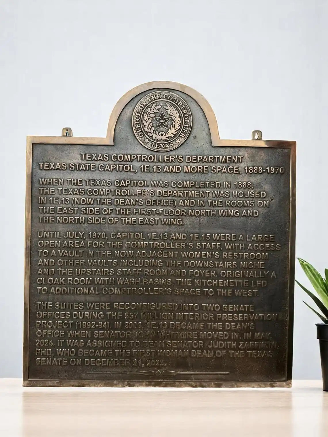 Bronze plaque with engraved text and a seal on a white background