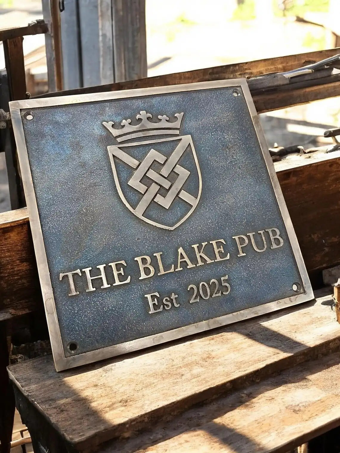 Bronze sign for The Blake Pub with a crest design on a wooden surface.