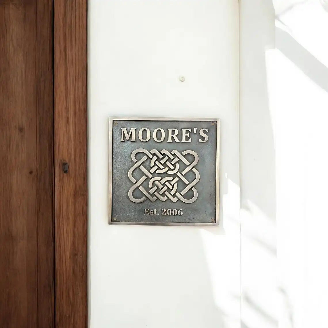Decorative Bronze sign with 'MOORE'S' and a Celtic knot design on a white wall.