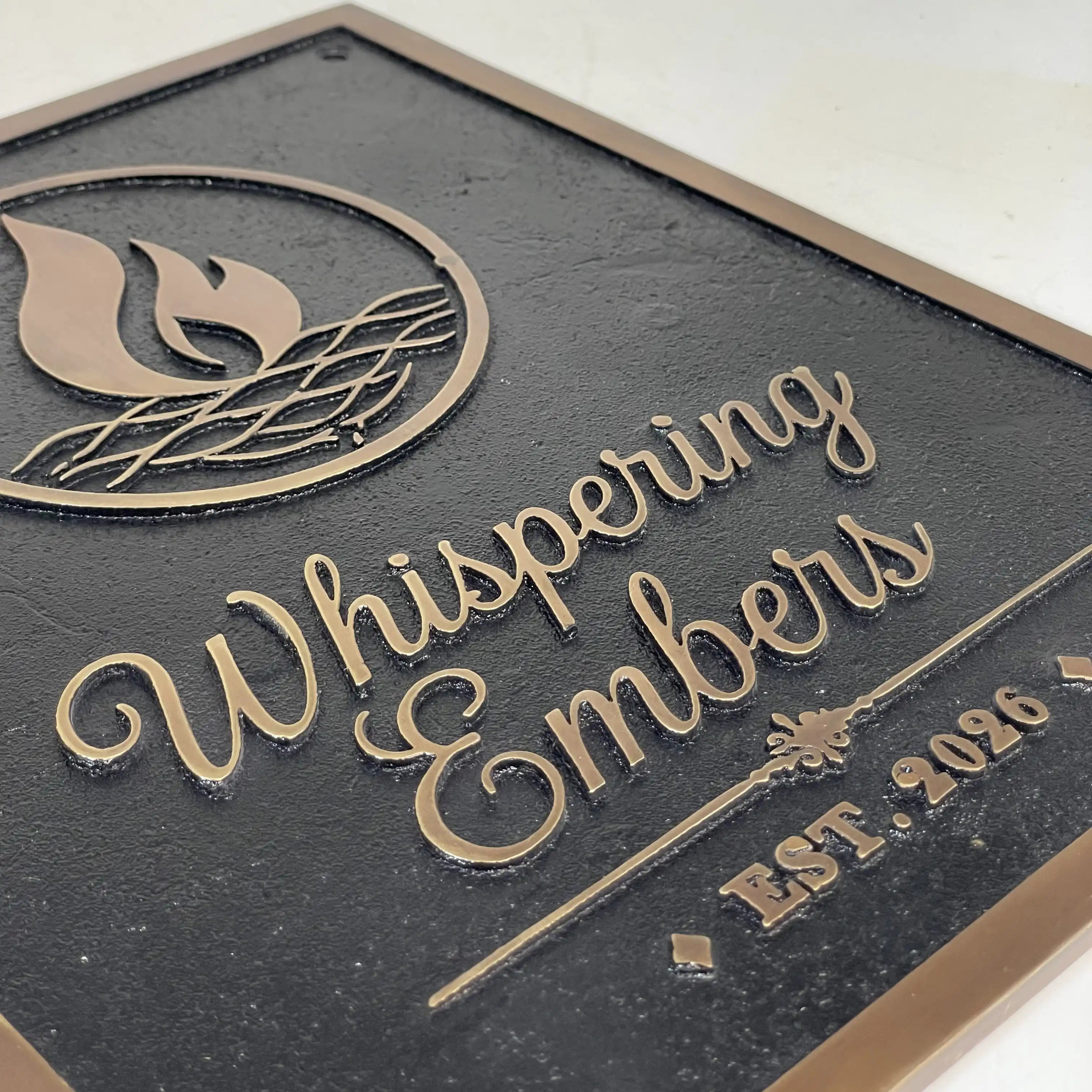 Cast bronze sign with 'Whispering Embers' logo and text raised on a dark background