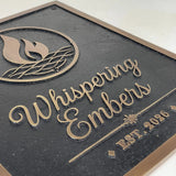 Cast bronze sign with 'Whispering Embers' logo and text raised on a dark background