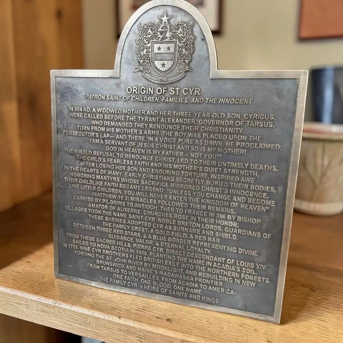 Metal plaque with engraved text and a crest on a wooden surface