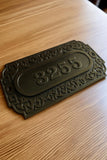 Decorative house number plate with '3255' on a wooden surface
