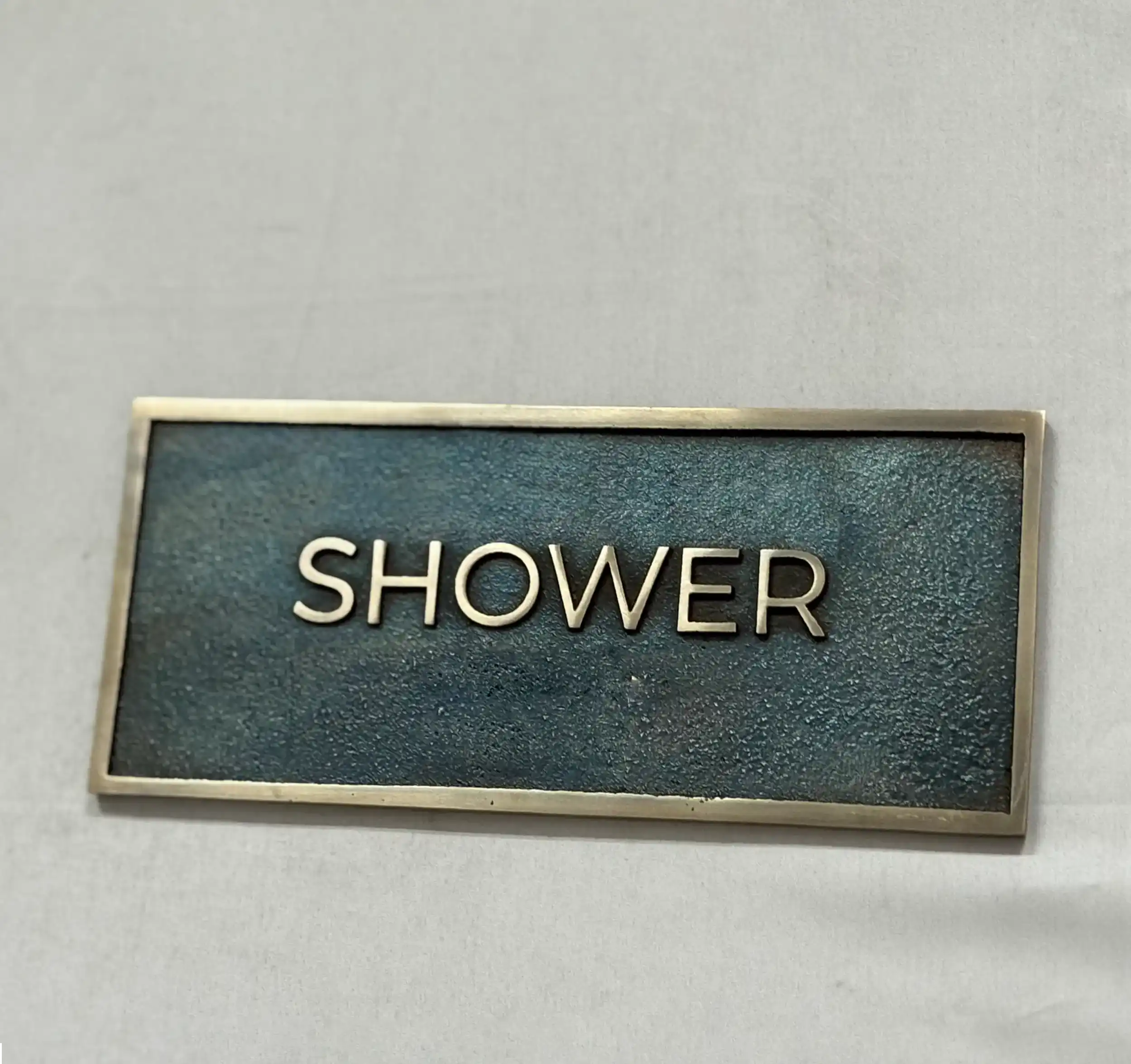Rectangular metal sign with 'SHOWER' text on a gray background
