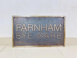 Metal sign with 'Farnham Eye Care' text on a white background