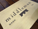 Brass sign with 'middleman' and 'NASH' text on a wooden surface