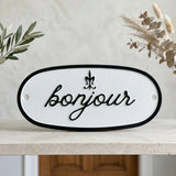 Address sign with 'bonjour' text on a shelf with plants