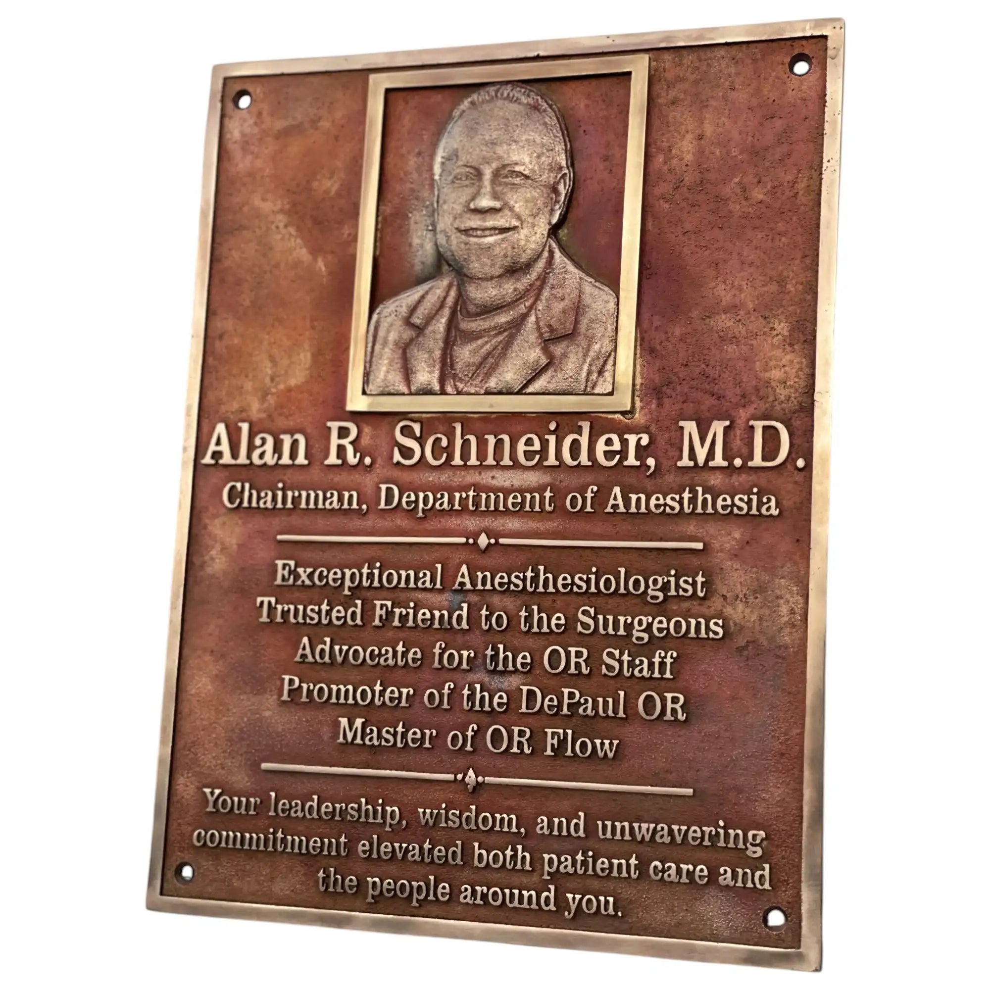 Bronze plaque with a portrait of Alan R. Schneider, M.D., and engraved text on a white background.