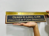 Nameplate with engraved text held by a hand against a white background