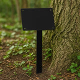 Black metal sign on a stand against a tree in a forest setting